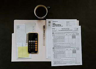 Die Spekulationssteuer und Spekulationsfrist beim Immobilienerwerb und Immobilienverkauf black Android smartphone near ballpoint pen, tax withholding certificate on top of white folder